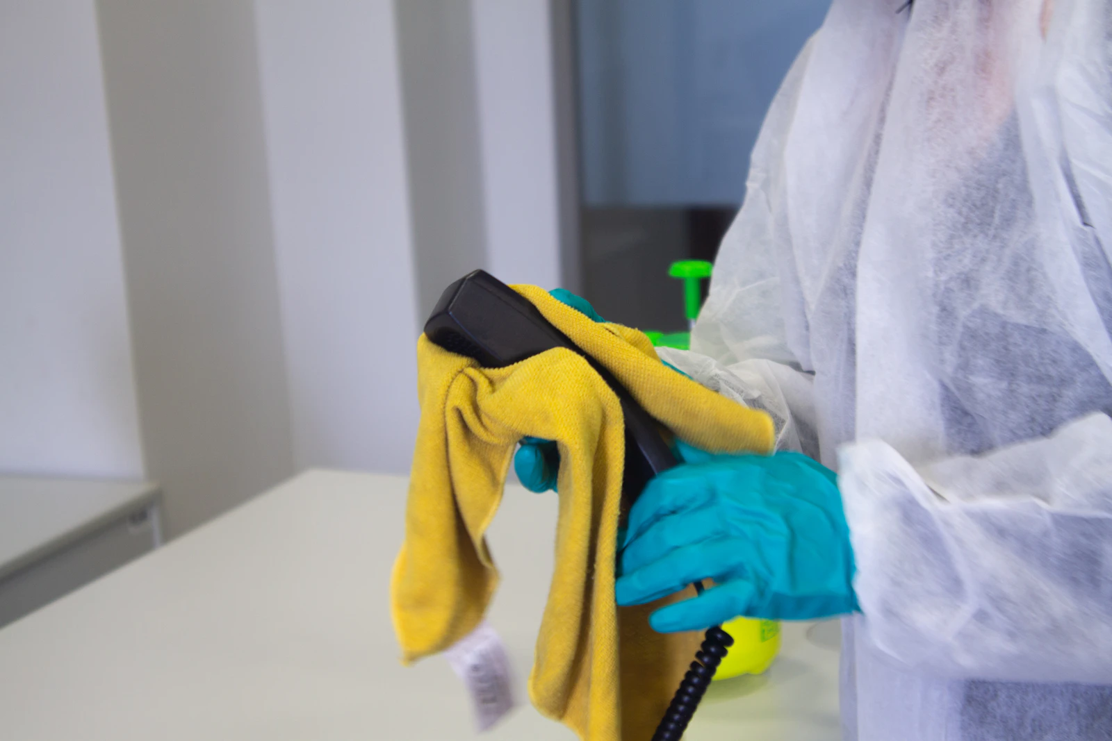 Fachkraft in Schutzkleidung wischt eine Fläche mit Tuch und Sprühmittel