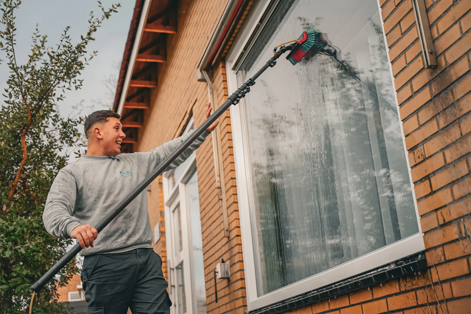 Glasreiniger säubert ein Fenster mit Teleskopstange und Abzieher