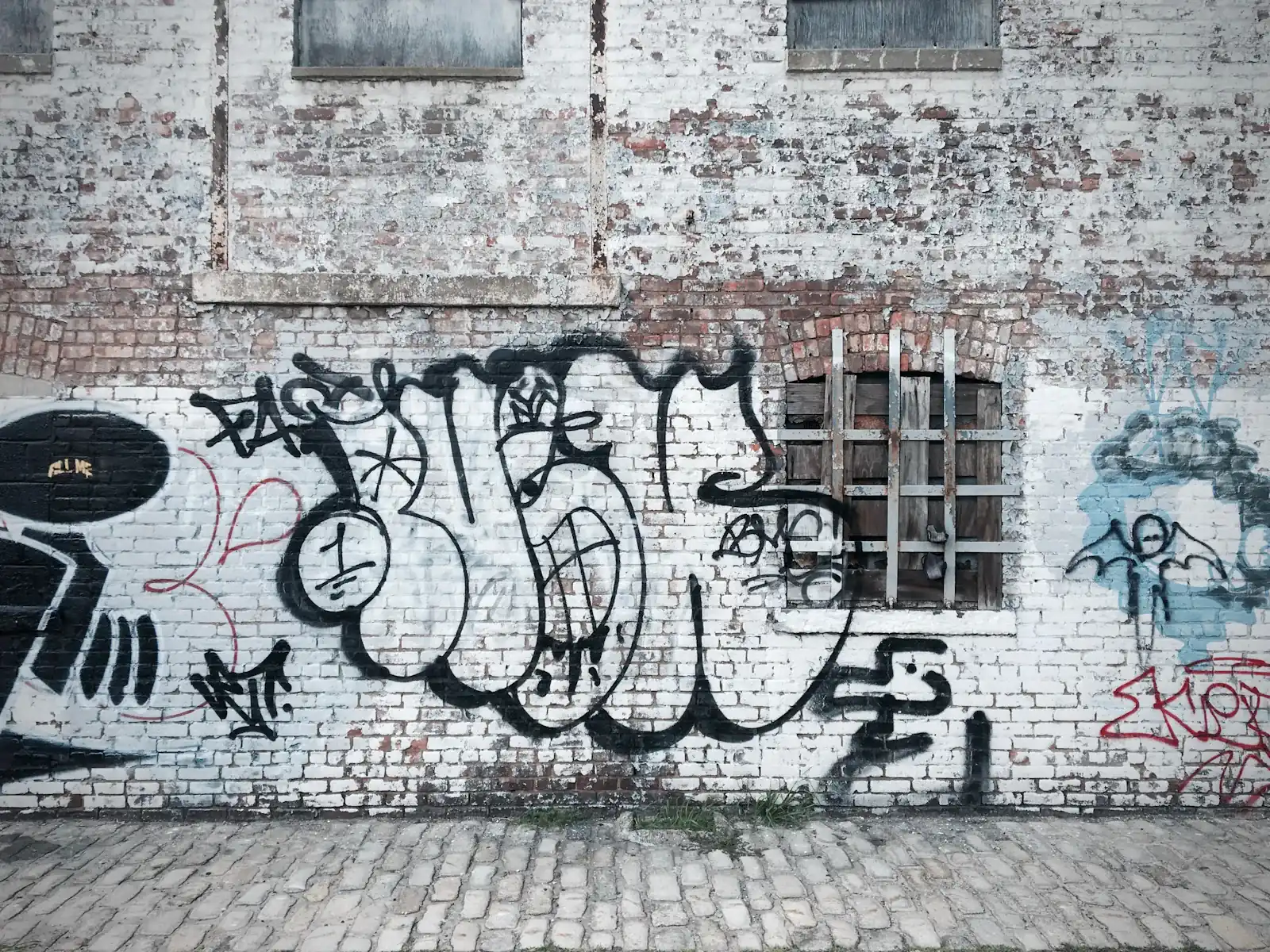 Mit Graffiti besprühte Ziegelwand an einer gepflasterten Gasse