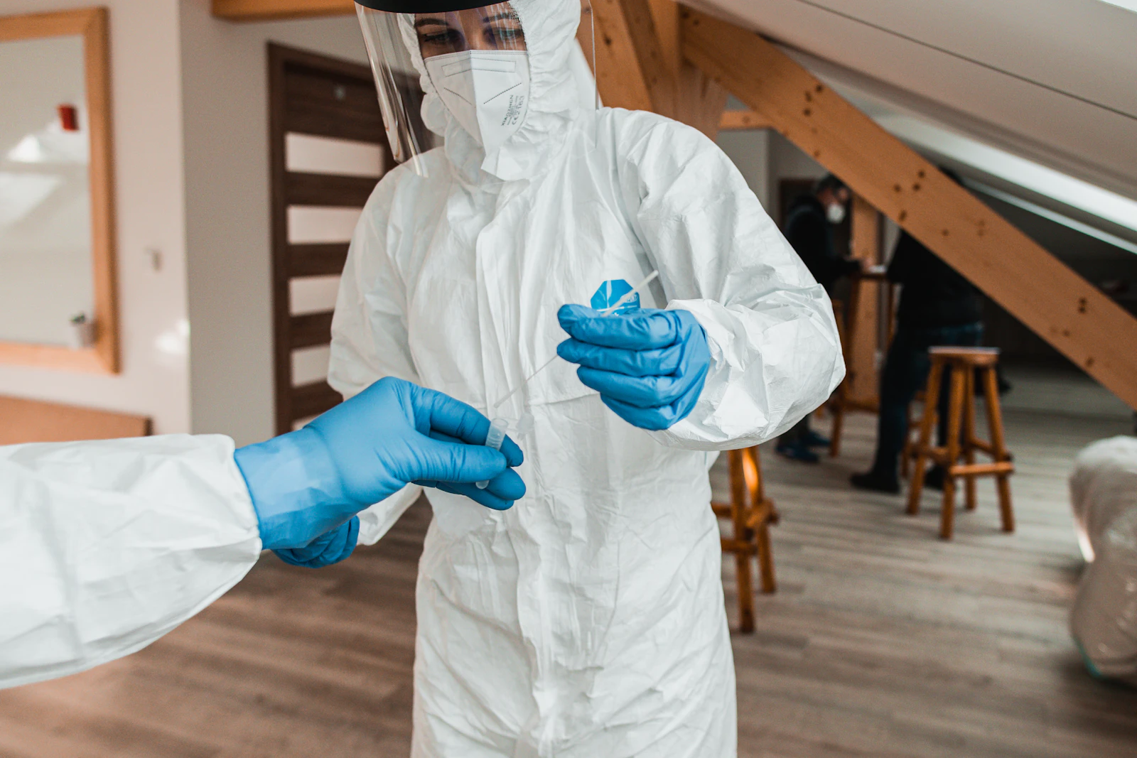 Fachkraft legt einen weißen Schutzanzug mit Handschuhen und Visier an